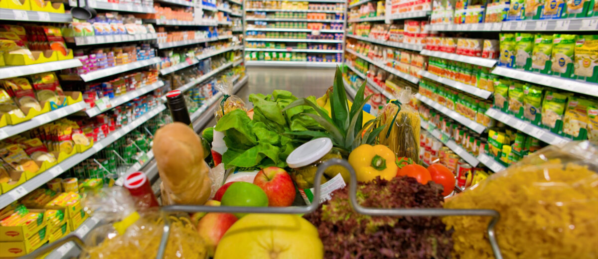 a shopping cart standing in a corridor of a supermarket in the stacks.